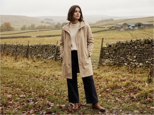 Woman in a cream country raincoat standing in an autumn field
